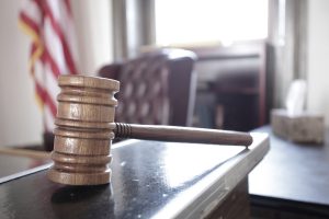 Court Room Gavel Sits on Desk with American Flag in the Background