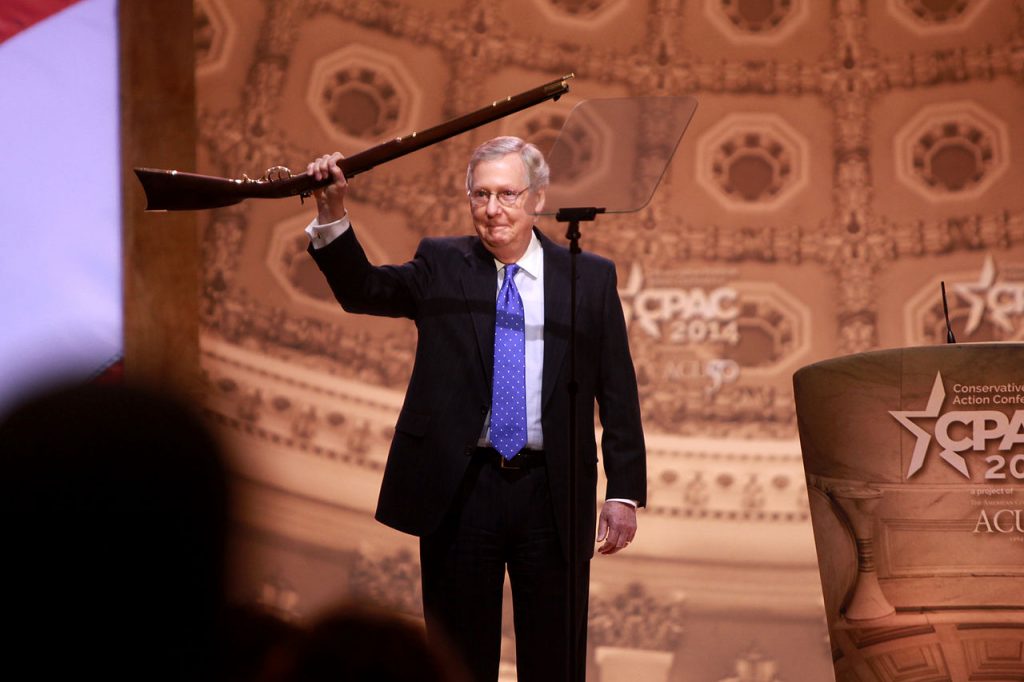 Mitch McConnell hoist a large gun over his head, celebrating like a Tusken raider.